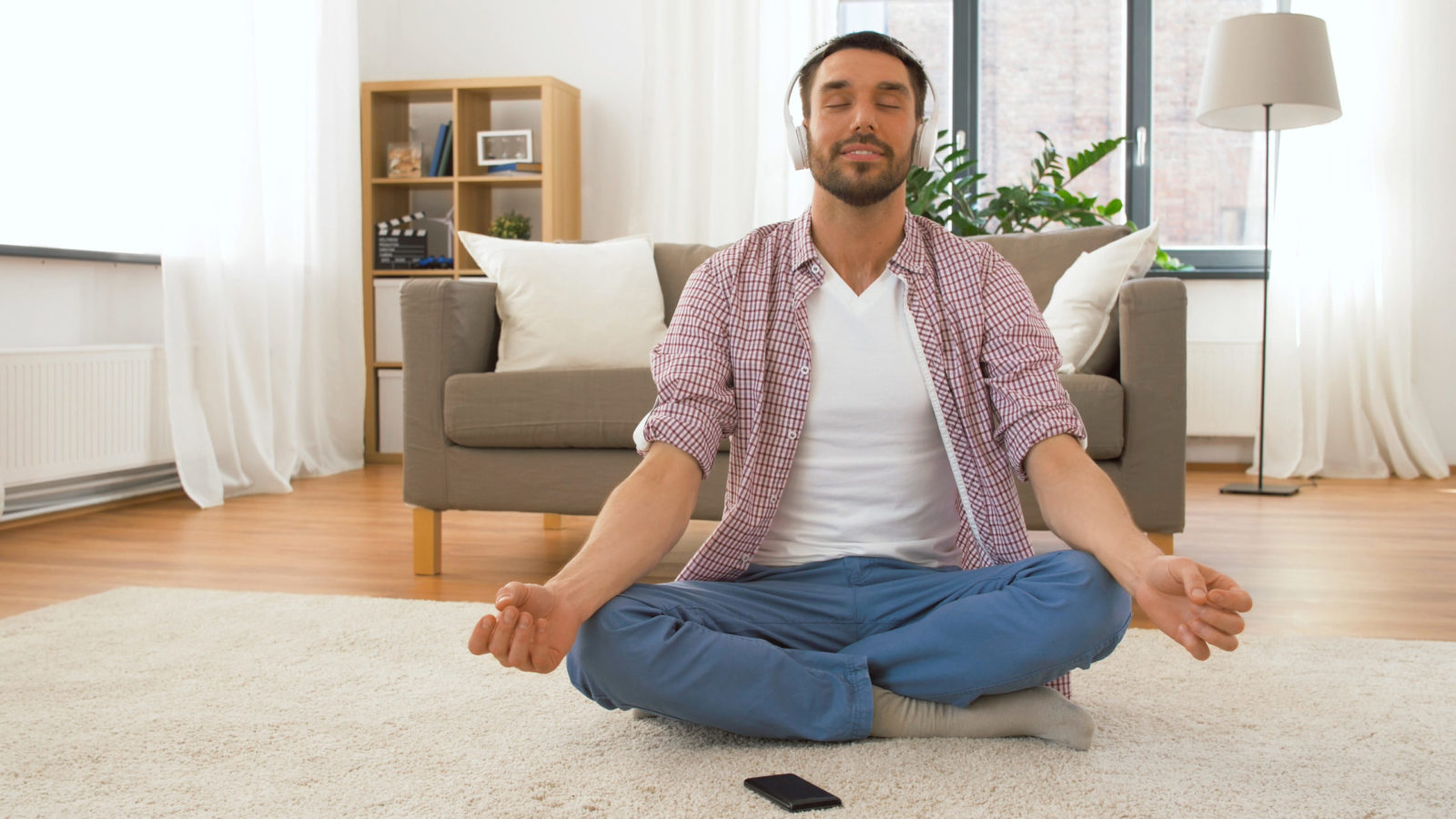 Man in headphones meditating in lotus pose at home
